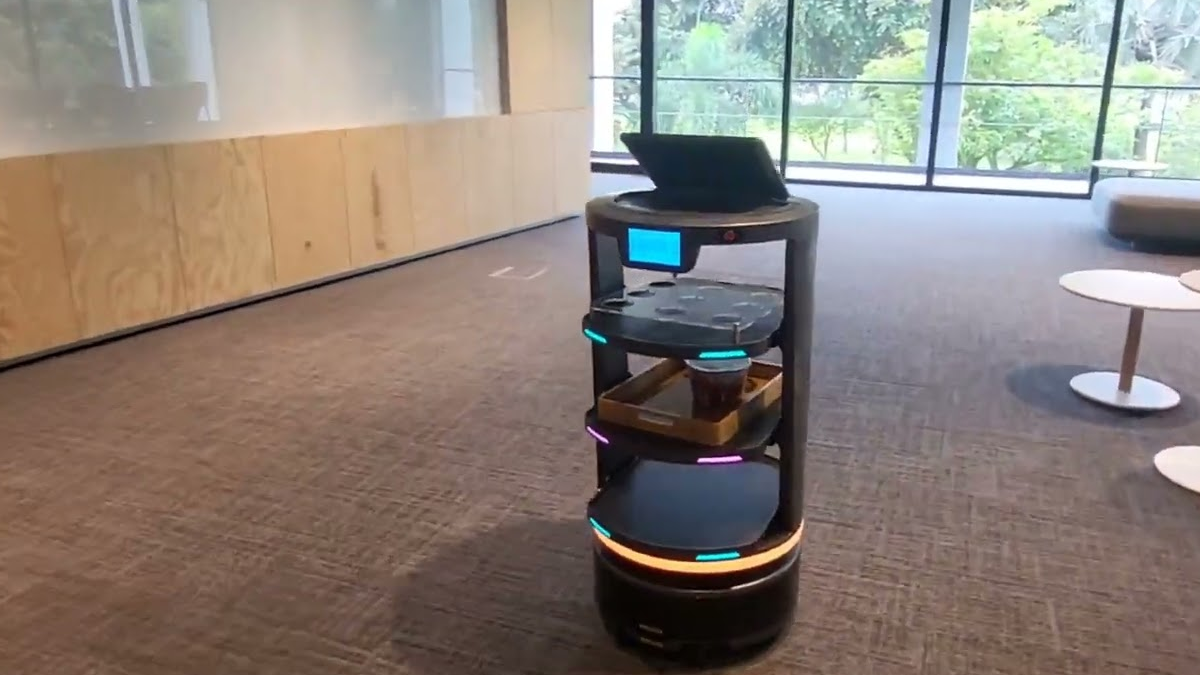 Autonomous delivery robot with multiple shelves and colorful LED rings in a modern lobby.