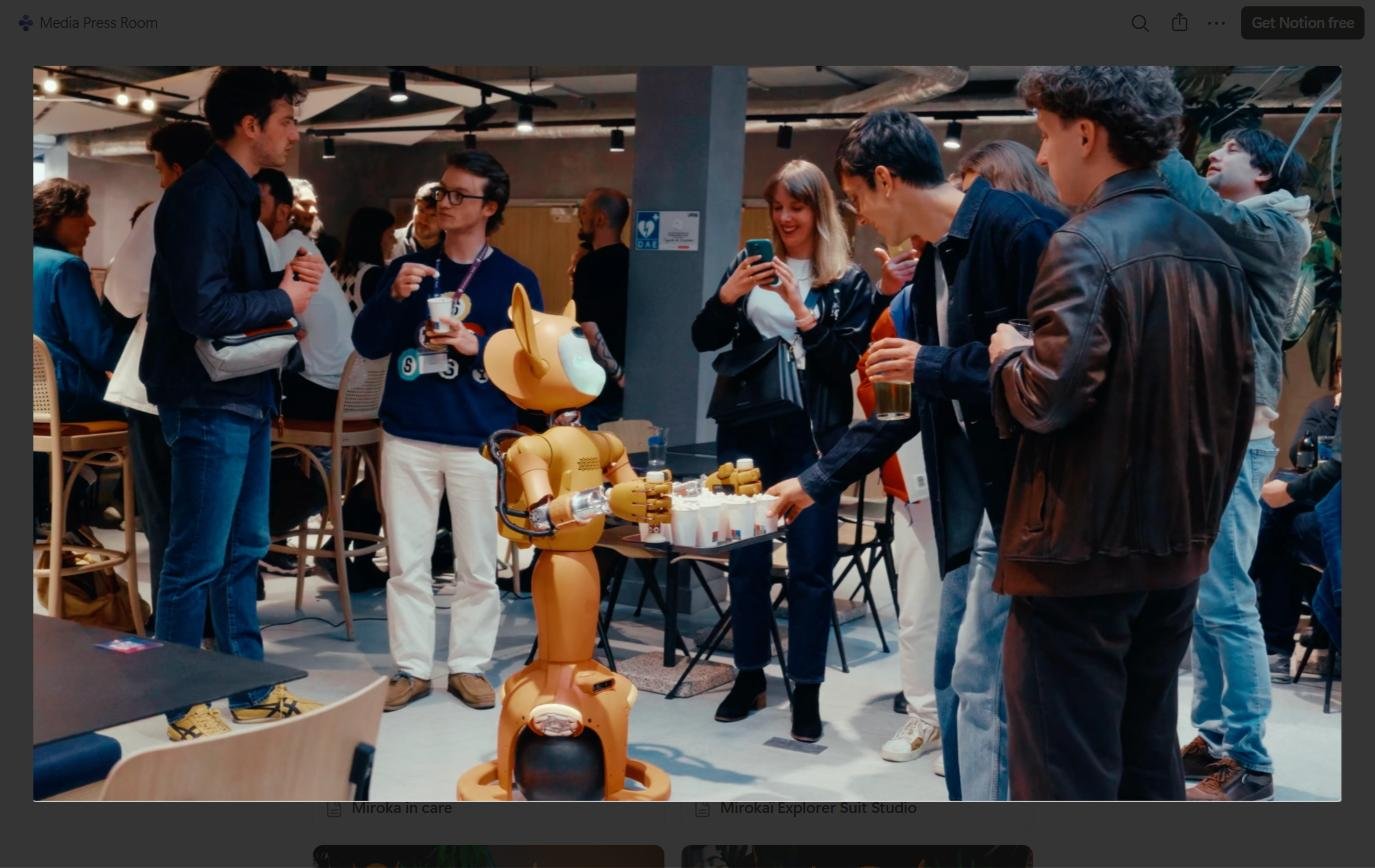 Crowd of people at a tech event gathered around an orange humanoid robot serving drinks.