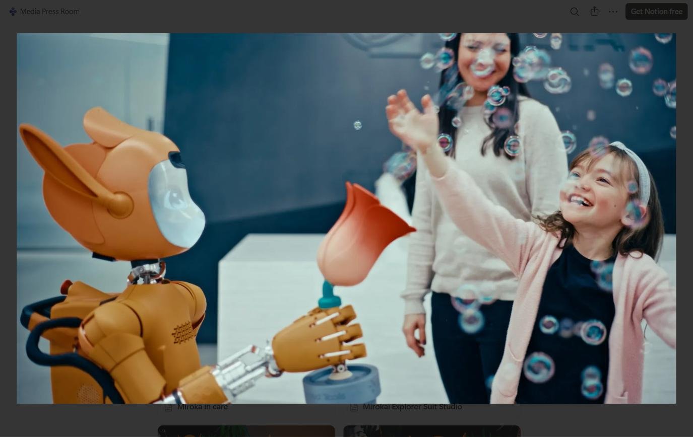 Orange robot hands a bubble wand to a smiling girl as bubbles float around indoors.